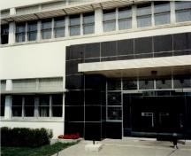 Vue de l'entrée principale du bâtiment M-20, qui montre l’emploi de matériaux « modernes » lisses comme l’acier, les blocs de verre, le stuc blanc et le parement de marbre noir, 1991.; Parks Canada Agency / Agence Parcs Canada, J. Adell, 1991.