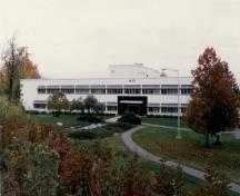 Vue générale du bâtiment M-20, qui montre la volumétrie basse, avec un bloc principal de deux étages flanqué de trois blocs de trois étages, le tout coiffé d’un toit-terrasse, 1990.; National Research Council of Canada / Conseil national de recherches du Canada, 1990.