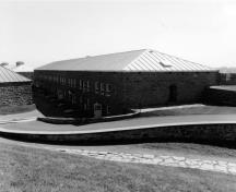 View of the exterior of Building 8, showing the simple, squat, plain rectangular massing and the hipped roof covered with painted sheet metal.; Parks Canada Agency / Agence Parcs Canada.