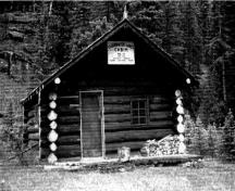 Front elevation of the Clearwater Lakes Warden Cabin, showing its six-pane windows with their muntin bars and the wood plank door, 1993.; Parks Canada Agency / Agence Parcs Canada, 1993.