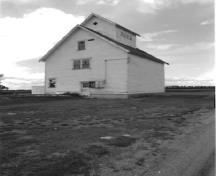 View of the Grain Elevator 22, showing the sloped-shoulder profile and two-and-a-half storey, gable-roofed massing with a projecting central cupola, 1993.; Department of Agriculture and Agri-Food / Ministère de l'Agriculture et de l'Agroalimentaire, 1993.