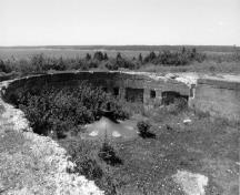 Vue générale de l'emplacement des pièces à fort McNab, qui montre la silhouette basse, partiellement souterraine de cet ouvrage en béton armé de conception utilitaire et fonctionnelle, 1996.; Agence Parcs Canada / Parks Canada Agency, I. Doull, 1996.