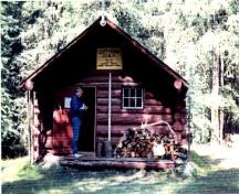 View of the front entrance of the Cuthead Warden Cabin, showing a low-pitched roof, gabled ends and a sheltered off-centered entrance porch with verandah, 1996.; Parks Canada Agency / Agence Parcs Canada, 1996.