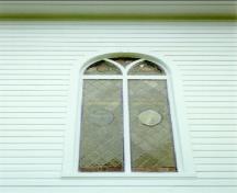 Detail of St. Peter's Anglican Church, showing a stained glass window and the white wooden planking, 1992.; Agence Parcs Canada / Parks Canada Agency, André Charbonneau, 1992.