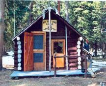 View of the main entrance to the Sandhills Warden Cabin, showing the entrance door to one side counterbalanced by a window, 1996.; Agence Parcs Canada / Parks Canada Agency, 1996.