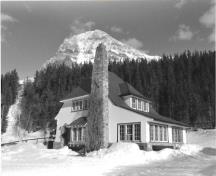 Side elevation of the Superindendent's Residence, showing the steeply pitched hipped-roof and massive, irregularly placed fieldstone chimney, ca 1965.; Agence Parcs Canada / Parks Canada Agency, ca./vers 1965.