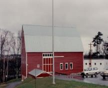 Vue de la façade latérale de la Station de recherche, qui montre le revêtement de planches à clin étroites, peintes en rouge, qui fait contraste avec les moulures peintes en blanc et la toiture en métal, 1993.; Agriculture Canada / Ministère de l'Agriculture, 1993.