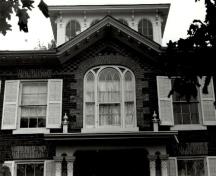 Vue en détail de la fenêtre dans la façade principale de la maison Bentley, qui montre le belvédère qui surmonte la maison, avec ses fenêtres en plein cintre et son toit à consoles, 1973.; Agence Parcs Canada / Parks Canada Agency, 1973.