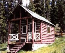 Corner view of Medicine Tent Warden Cabin, showing its log-framed sheltered porch area at the entrance gable, 1996.; Parks Canada Agency / Agence Parcs Canada, 1996.