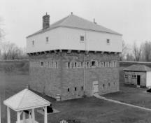 Corner view of the Blockhouse, showing the square, three-storey massing with pyramidal roof, and the chimneys, 1991.; Parks Canada Agency / Agence Parcs Canada, 1991.