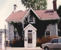 Vue de la façade du bâtiment 6 du CMR, qui montre les détails d’ornementation en bois que présentent encore les portes, les châssis des fenêtres, la fasce et l’avant-toit, 1993.; Parks Canada Agency / Agence Parcs Canada, 1993.