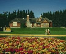 Vue panoramique de l'édifice administratif du parc démontrant la conservation de la relation initiale entre l’édifice et la route ainsi qu’avec les jardins aménagés, les arbres matures et les pelouses du parc central, 1986.; Parks Canada Agency / Agence Parcs Canada, Barrett & MacKay, 1986
