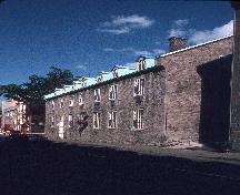 Corner view of the St. Louis Street front showing the consistent detailing including multi-pane casement windows, overlit doors set at street level, and contrasting stone quoins and sill.; Parks Canada Agency / Agence Parcs Canada, n.d.