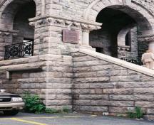 Detail view of of St. John's Court House's entrance showing the plaque as well as its stone staircase, and arched portico with decorative stonework including voussoirs, keystone, columns, balustraded balcony and carved motifs, 2005.; Parks Canada Agency / Agence Parcs Canada, 2005.