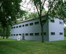 General view of Butler's Barracks showing the Soldiers’ Barracks in its rectangular, two-storey massing under low, hipped roof, brick wall infill, and regularly placed, horizontally shaped windows, 1994.; Parks Canada Agency / Agence Parcs Canada, B. Morin, 1994.