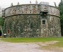 Vue générale de la Tour Martello Prince-de-Galles montrant les murs de maçonnerie circulaires massifs et le mur extérieur qui s’incline légèrement vers l’intérieur à mesure qu’il gagne en hauteur, 1995.; Parks Canada Agency / Agence Parcs Canada, 1995.