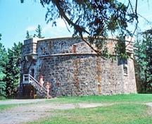 Vue générale du tour martello Prince-de-Galles montrant le volume géométrique simple de la tour de pierres au profil cylindrique trapu, 1977.; Parks Canada Agency / Agence Parcs Canada, T. Grant, 1977.