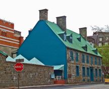 Vue générale de la Maison Maillou qui montre sa toit très incliné à deux versants avec petites lucarnes à pignon et les cheminées en pierre, 2003.; Parks Canada Agency / Agence Parcs Canada, 2003.