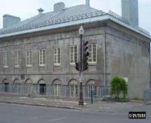 Corner view of the Old Québec Custom House, showing its ashlar exterior facing and its rectangular, two-storey massing under a low-pitched hipped roof with symmetrical end chimneys, 2002.; Parks Canada Agency / Agence Parcs Canada, 2002.