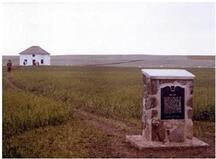 La plaque de Fort Pitt érigé par la province de Saskatchewan en 1973 avec la reconstruction de la maison du facteur en chef à l’arrière plan.; Parks Canada / Parcs Canada,