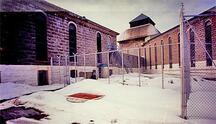 General view of the main cellblock at Saint-Vincent-de-Paul Penitentiary showing the high, surrounding stone wall which provides the distinctive public face of the institution.; Parks Canada Agency / Agence Parcs Canada, n.d.