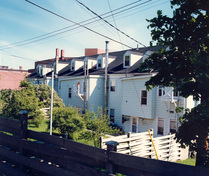 Rear view of the Dockyard Terrace, showing the building’s simple two-storey form and wide tripartite, rectangular massing with a gable roof, rear dormers and chimneys, 1986.; Department of National Defence / Ministère de la Défense nationale, 1986.