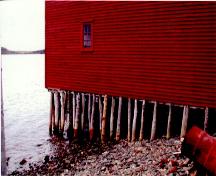 Exterior photo of Grant's Stage, Trinity, Trinity Bay, NL.  Photo showing wooden support posts as building extends over the water.; HFNL 2005