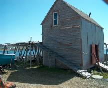 Exterior view of fish flake and of gable end and entrance side of the net store of Samuel Abbott Fishing Room, Newman's Point, Bonavista, NL, circa 2006; Bill Abbott/HFNL 2006
