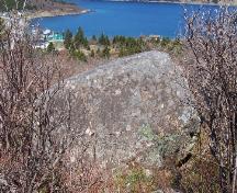 Southern side of Rock with 17th and 18th Century Graffiti showing Kingman's Cove, Fermeuse, NL in the background. Photo taken May 2006.; HFNL/Andrea O'Brien 2006