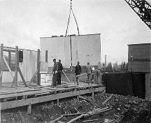 A crane manoeuvres a prefabricated wall into place for one of 100 houses built in 66 days in 1947.; Moncton Museum