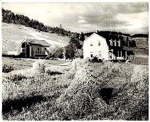 Cette image montre la façade nord de la maison ancestrale, en blanc. La galerie ornant la façade de la maison est également apparente.; ONEF :  "Vallée de la St-Jean" (1949)