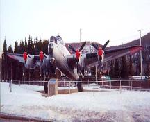 The Lancaster KB882 Aircraft as it appears today at its final location at the Edmunston Municipal Airport. Barracade ropes can be seen around the site. A commemorative plaque is situated in front of the plane.; Troy Kirkby