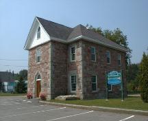 This corner view of the building presents the front projection around the central main entrance with a medium pitch roof and a front gable.; PNB 2004