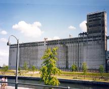 Vue générale de l'élévateur B1, qui montre l’échelle massive du bâtiment, sa volumétrie rectangulaire, les deux étages vitrés au sommet du bâtiment et la tour à l’extrémité ouest, 1995.; Parks Canada Agency / Agence Parcs Canada, J. Hallé, 1995.