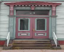 Cette image montre l'entrée avec un entablement à fronton, des consoles, des pilastres, un imposte et des portes doubles en bois présentant des panneaux de verre à arche segmentée, 2005; City of Saint John