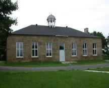 Cette image montre la façade principale symétrique de l’édifice rectangulaire construit de pierres surmonté en son centre d’une coupole.; PNB 2005