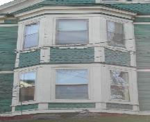 This image provides a view of the two-storey, off-centered bay window with fish-scale shingling in the spandrel panels between storeys, 2006; City of Saint John