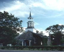 Vue de l'extérieur de l'église anglicane St. Stephen, qui montre la flèche à trois étages et la porte à deux vantaux surmontée d’une imposte semi-circulaire de l’entrée principale, 1992.; Parks Canada / Parcs Canada, 1992.