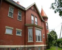 This photograph illustrates the dominant gable, the single storey bay window, the rounded tower, as well as the sandstone sills, lintels and plinth band, 2007; City of Saint John