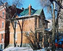 This view of the south facade of the Foote Residence illustrates its prominent orange brick construction and painted embossed metal roof, with corbelled chimney.; City of Edmonton, 2004
