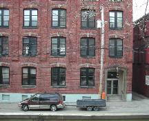 This photograph displays the style of the windows, the north entrance, and the projecting course of bricks that runs vertically through the top four floors, 2004.; City of Saint John