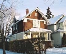 This image illustrates the two storey west and south wood-clad facades with  front and rear gables, side dormer, soffit support brackets, corner 'eye' windows and full-width hipped-roof veranda.; City of Edmonton
