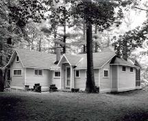 General view of Kingswood Cottage, showing the wood construction clad in horizontal wood siding and the gabled entrance portico decorated with wood trellis, 1984.; Parks Canada Agency / Agence Parcs Canada, M. Trépanier, 1984.