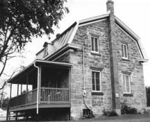 Vue générale de la maison du percepteur, qui montre la volumétrie basse sur deux étages avec des murs pignons relativement amples et le toit à comble brisé percé de lucarnes, 1989.; Parks Canada Agency / Agence Parcs Canada, 1989.