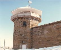 View of Tower D-2, showing the stone work that includes wider blocks for the flared base, smaller blocks higher up and smooth stones for the corner quoins, 1990.; Correctional Services Canada / Service correctionnel du Canada, 1990.