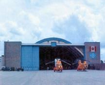 View of the exterior of 9 Hangar, showing the elevation with its large doors that slide into massive rectangular brick-clad pocket towers, and the smaller openings at its apex intended for taller aircraft tail assemblies, 2003.; Department of National Defence / Ministère de la Défense nationale, 2003.