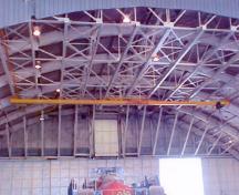 View of the interior of 9 Hangar, showing the long span, three-hinged segmented steel truss arches which frame the roof, 2003.; Department of National Defence / Ministère de la Défense nationale, 2003.
