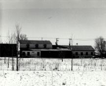 Vue de l’atelier de menuiserie, qui montre la forme extérieure du bâtiment, qui évoque la nature transitoire de nombre des activités qui s’y sont déroulées ainsi que sa fonction d’atelier, 1989.; Agence Parcs Canada / Parks Canada Agency, 1989.