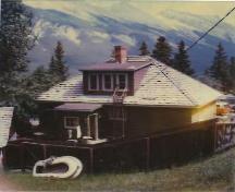 Rear view of the Upper Hot Pool Residence, showing its one-and-a-half storey structure of standard platform frame construction, with a rectangular plan and medium-pitch gable roof, 1990.; Parks Canada Agency / Agence Parks Canada, 1990.