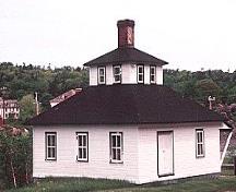 General view of Building 18, showing the single-storey square massing with hipped roof, the lantern and the large, central, corbelled brick chimney, circa 2004.; Parks Canada Agency / Agence Parcs Canada, circa / vers 2004.